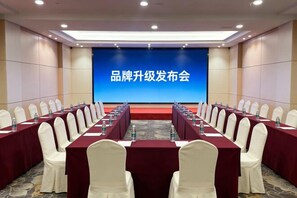A conference room with rows of tables and chairs, a large screen displaying text, and a carpeted floor. - Green Jinyi hotel (Nanchang)