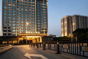 A hotel entrance with a sign, a road with directional arrows, and a tall building in the background. - Green Jinyi hotel (Nanchang)