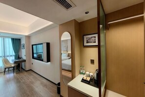 A hotel room with a bed, a desk, a chair, a mirror, a television, and a small table with toiletries. - Green Jinyi hotel (Nanchang)