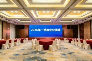 Ein Konferenzraum mit einer großen Leinwand, die Text zeigt, runden Tischen mit Stühlen und einem Teppichboden.