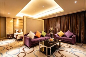 Habitación de hotel con sofá, una mesa de centro, cama y un gran ventanal con cortinas.