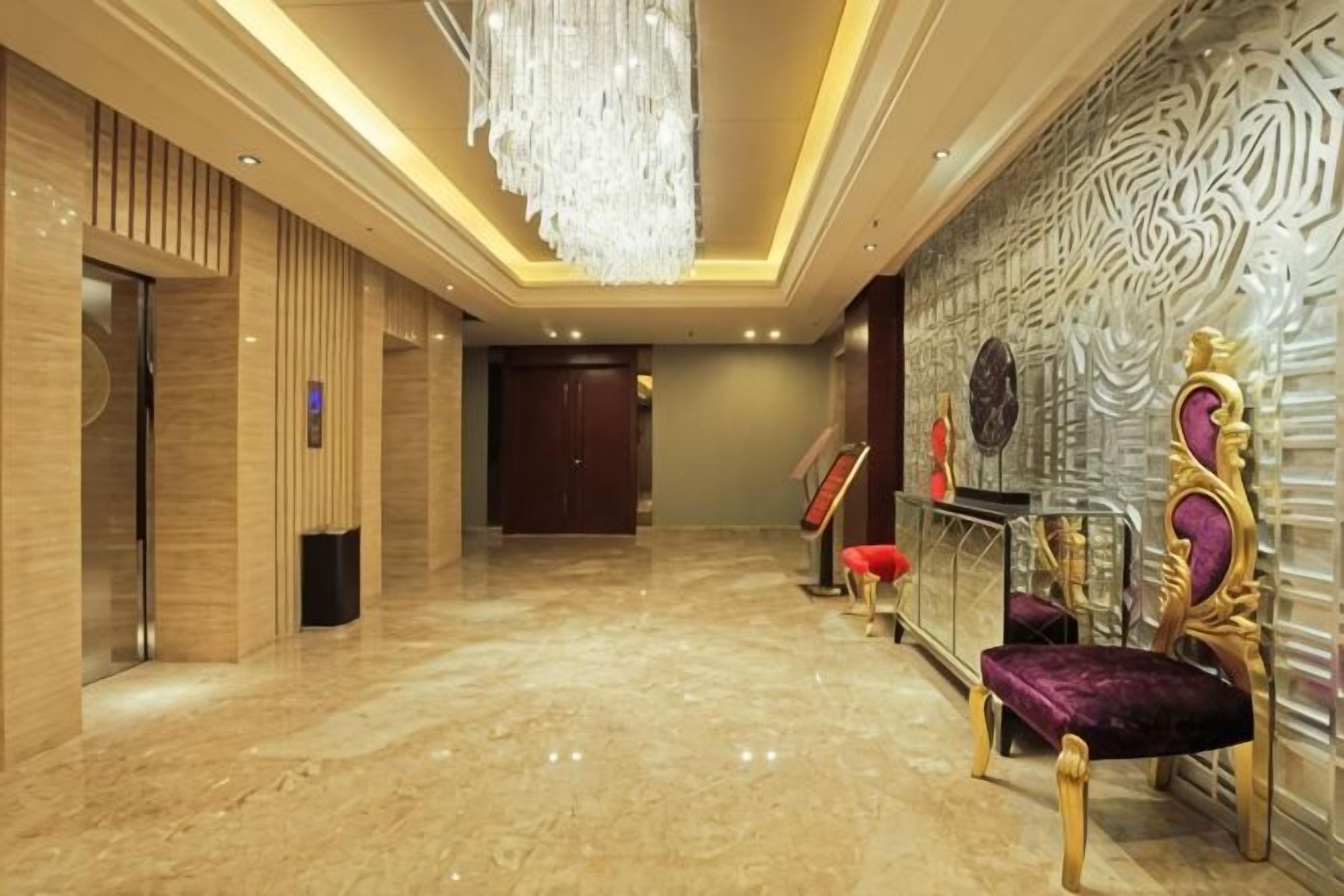 A hotel lobby with a marble floor, a chandelier, a reception desk, and a wall with an intricate design.