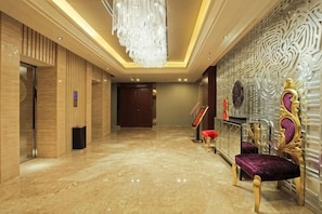 Un vestíbulo de hotel con piso de mármol, un candelabro, una mesa de recepción y una pared con diseño ornamental.