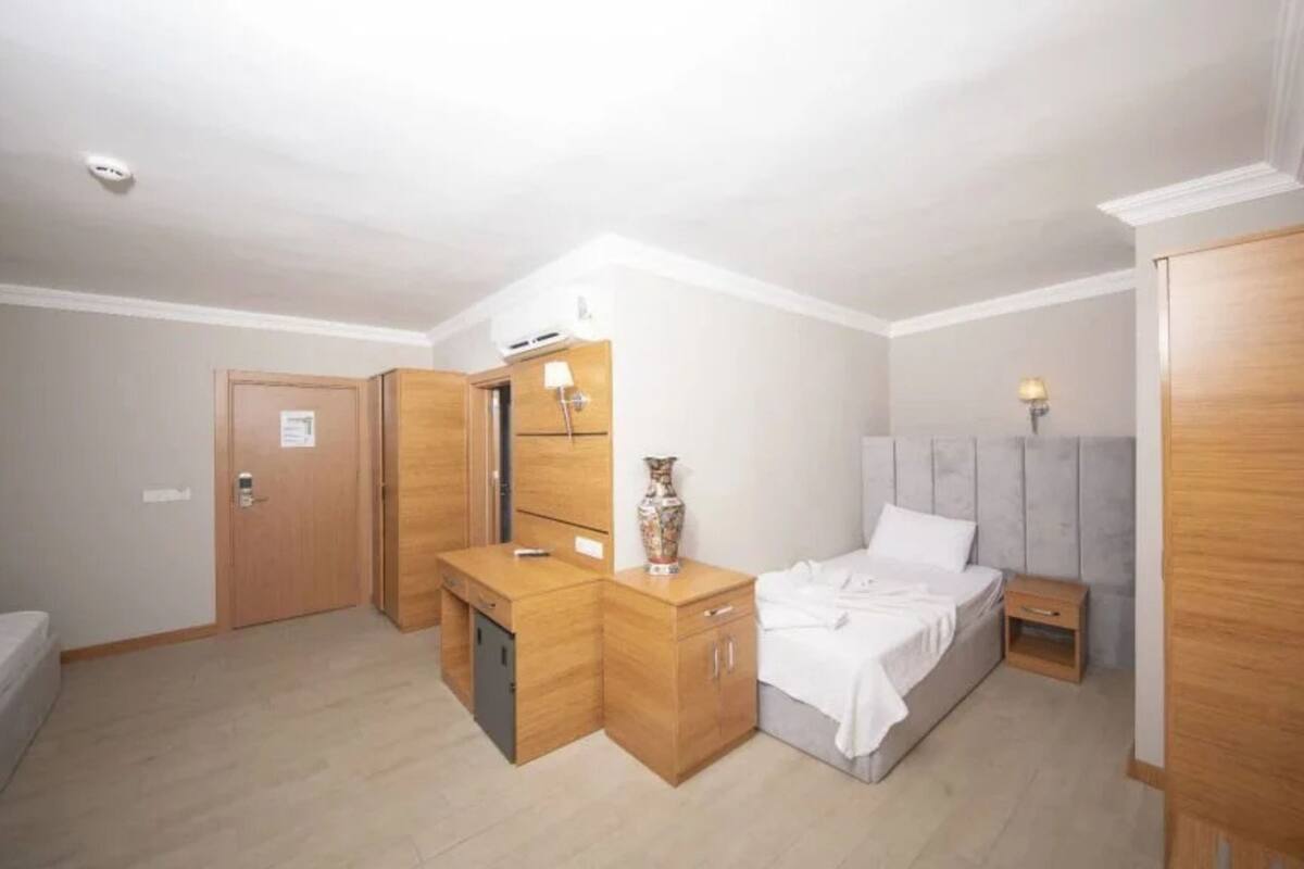 A bedroom with a bed, bedside table, wardrobe, and a small desk with a lamp.