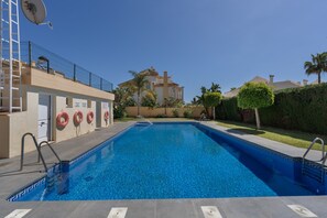 Une piscine à l’eau d’un bleu limpide, entourée d’une clôture, et un bâtiment avec un balcon en arrière-plan.