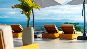 Un área de lounge en la azotea con sillones de madera, una planta en maceta y sombrillas para dar sombra.