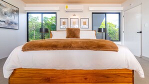 Un dormitorio moderno con una cama grande, un cabecero de madera y vistas a zonas verdes por las ventanas.