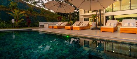 A swimming pool with lounge chairs and umbrellas, surrounded by lush greenery and modern architecture.