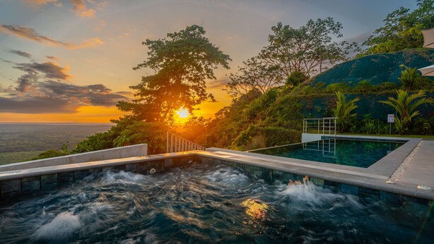 Una piscina de aguas termales con vista al atardecer y follaje circundante.