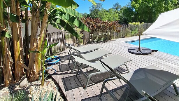 Una terraza de madera con sillones de descanso y una piscina.