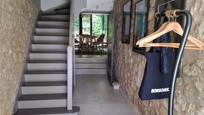 Un pasillo con una escalera, un perchero de madera y un bolso negro con la etiqueta 'BONSOIRS'.