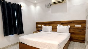 A hotel room with a bed, a wooden headboard, an air conditioning unit, a nightstand, and a window with curtains.