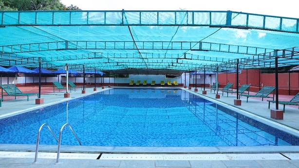 A swimming pool with a blue water surface, surrounded by green chairs and a covered area with a blue canopy.