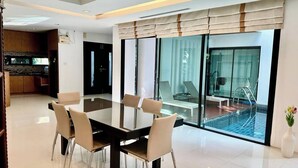 Moderni hotellihuone, jossa on ruokailutila, keittiö ja lasiseinöin varustettu uima-allas.