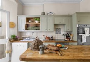A kitchen with light green cabinets, a wooden countertop, a dishwasher, and various kitchen items. - Haremere Hall - A Jacobean Estate of Grandeur (Etchingham)