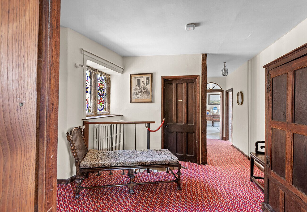 A hallway with a patterned carpet, a bench, a wooden door, and a stained glass window.