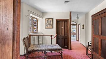 A hallway with a patterned carpet, a bench, a wooden door, and a stained glass window.