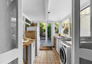 Cocina compacta con lavadora, un lavabo y ventana con vistas a un jardín.