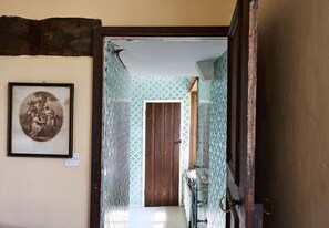 Un pasillo estrecho con una puerta de madera, un cuadro enmarcado en la pared y un baño con papel tapiz estampado y un espejo.