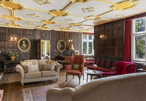 Ein Zimmer im klassischen Stil mit einer großen Wandpaneelaus Holz, einem roten Sessel, einem beigen Sofa und einem roten Samtsofa.