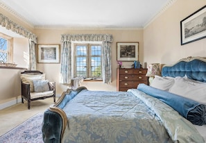 A bedroom with a large bed, a dresser, a chair, and a window with curtains.