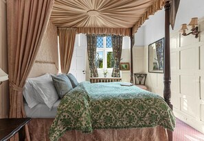 Un dormitorio con cama con dosel, una mesita de noche y una ventana con cortinas.