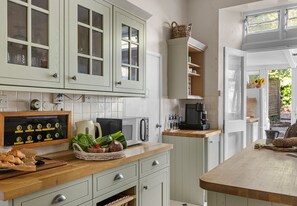 Cocina con armarios blancos, microondas, cafetera y encimera de madera.