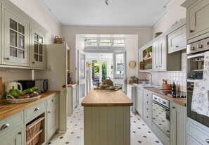Una cocina con isla central, armarios blancos y vistas a un jardín por una puerta abierta.