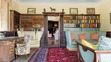 A library with bookshelves, a desk, a chair, a sofa, and a patterned rug.