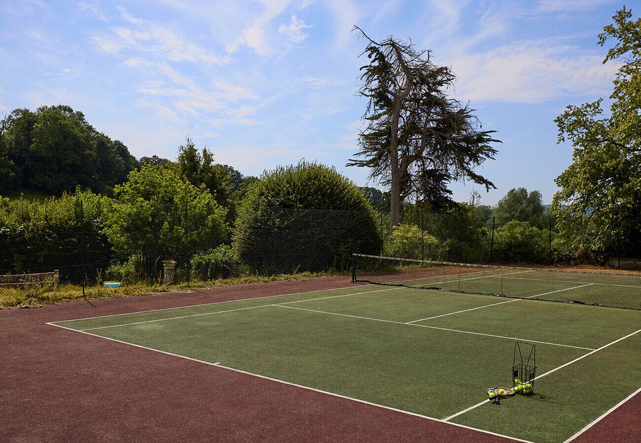 A tennis court with a net, surrounded by trees and a fence.