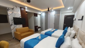 A hotel room with two beds, a sofa, a TV, and a wardrobe. - Niharika Heights Luxury Hotel (Bengaluru)