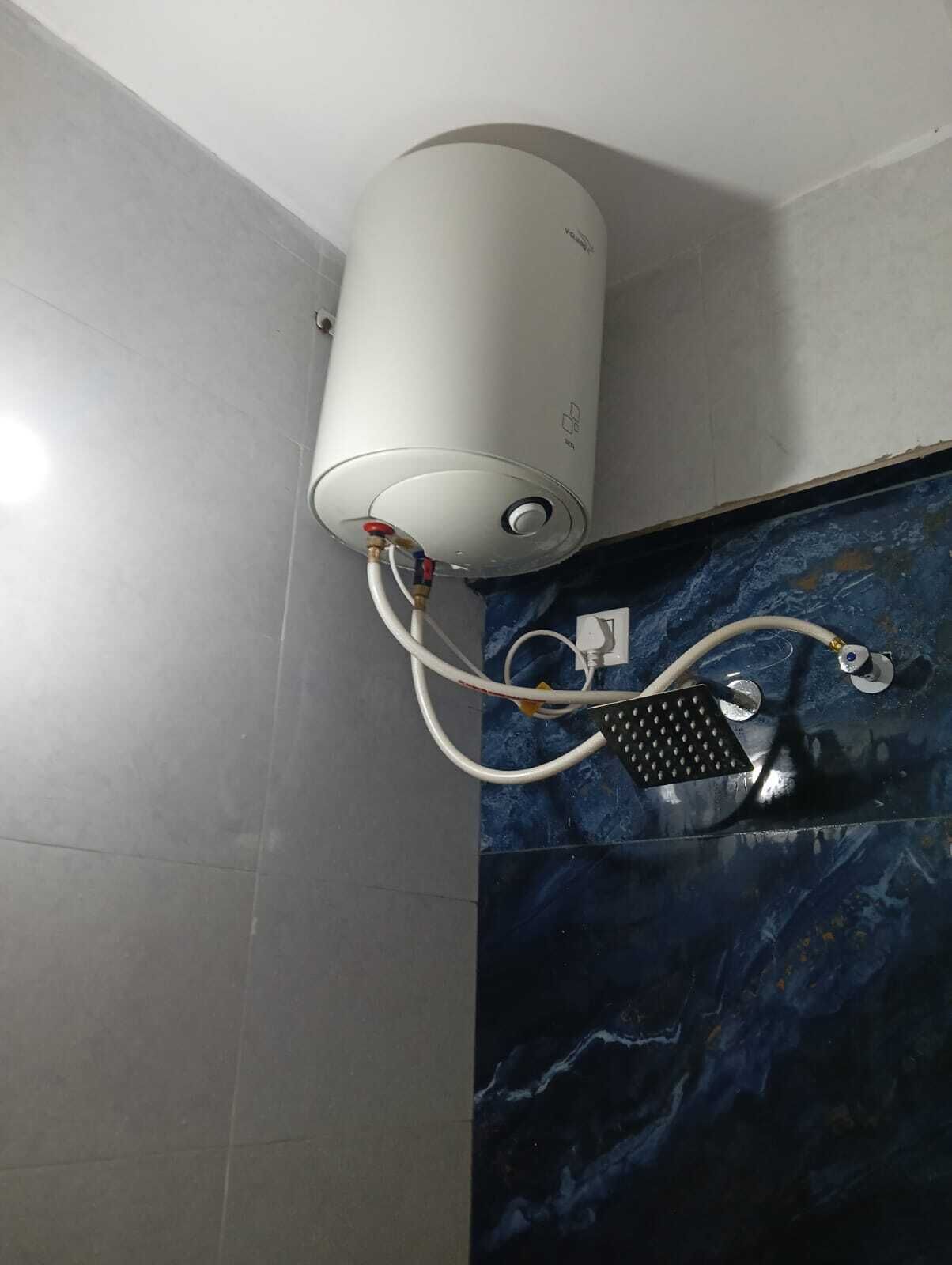 Een badkamer met een witte, cilindervormige boiler aan de muur bevestigd, verbonden met een douchekop.
