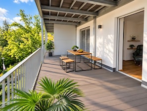 Un balcon avec une table et des bancs en bois, des plantes en pot et une vue sur les arbres.