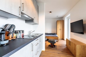 Eine moderne Küche mit einer Kaffeemaschine, einer Spüle und einer Arbeitsplatte. Es gibt ein Bett mit einem hölzernen Kopfteil und einen an der Wand befestigten Fernseher.