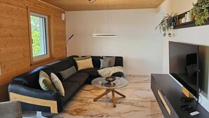 Een moderne woonkamer met een zwarte leren bank, een glazen salontafel, een flatscreen televisie en houten vloeren.