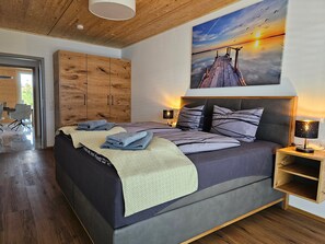 Un dormitorio moderno con una cama grande, cabecera de madera y un cuadro de una puesta de sol.