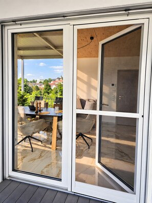 A modern sliding glass door leading to an outdoor patio with a dining table and chairs, a view of a residential area, and a wooden ceiling. - Deluxe Apartment Stadtblick 13 with Spacious Balcony and City View (Pfullendorf)