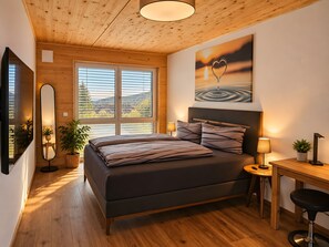 A modern bedroom with a large bed, a desk, and a view of the outdoors through the windows. - Deluxe Apartment Stadtblick 13 with Spacious Balcony and City View (Pfullendorf)