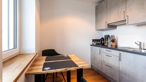 A compact kitchen with a wooden table, a black chair, and a built-in stove. - Premium Apartment City View 8 with XXL Balcony (Pfullendorf)