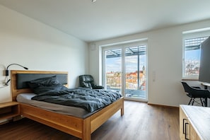 Una camera da letto moderna con un letto di legno, una sedia nera, una scrivania e un'ampia finestra vista città.