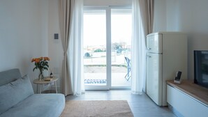 Habitació d'hotel moderna amb un llit, una taula petita amb flors, un refrigerador i una televisió.