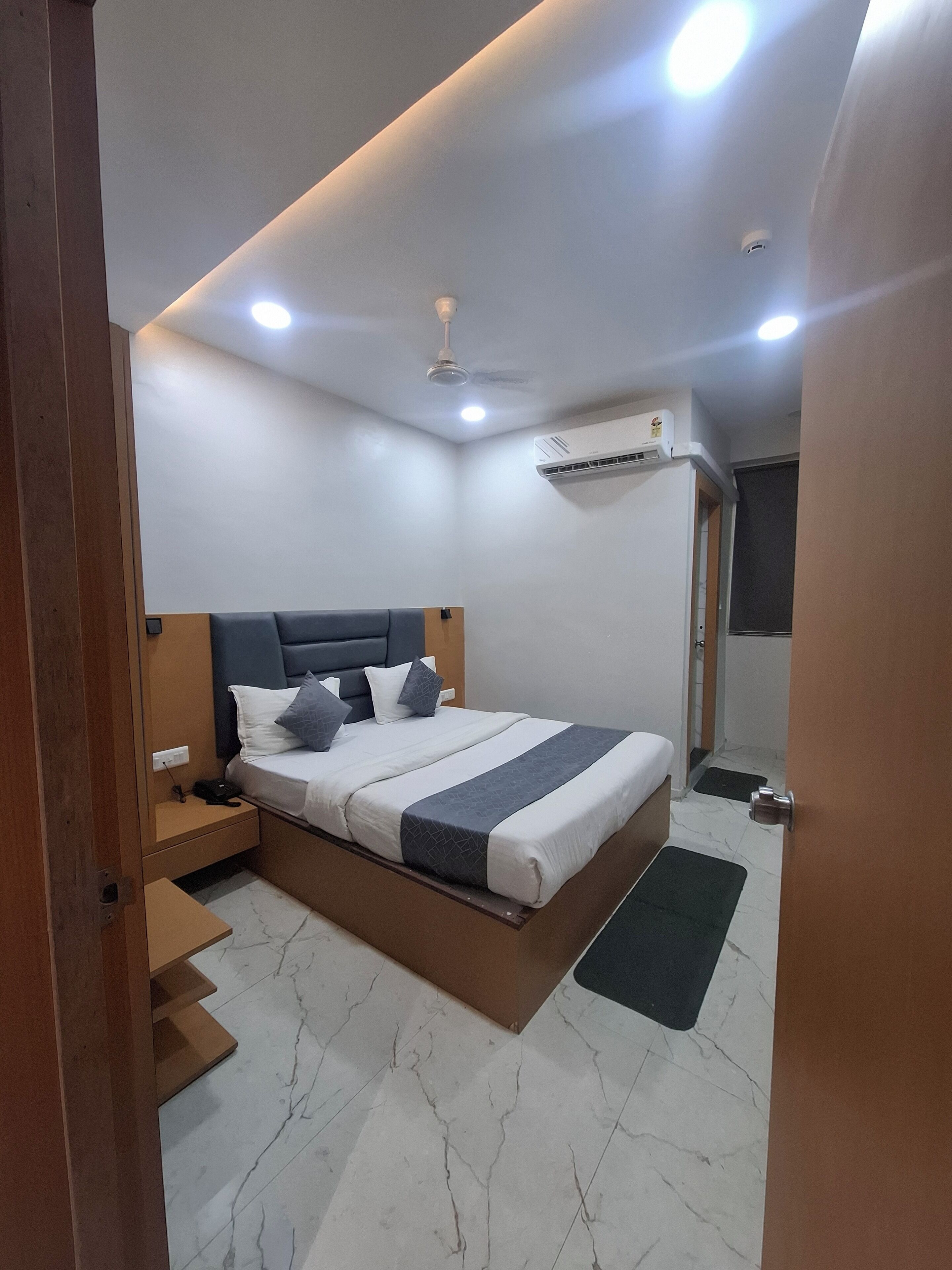A modern bedroom with a bed, bedside tables, an air conditioning unit, and a ceiling fan.