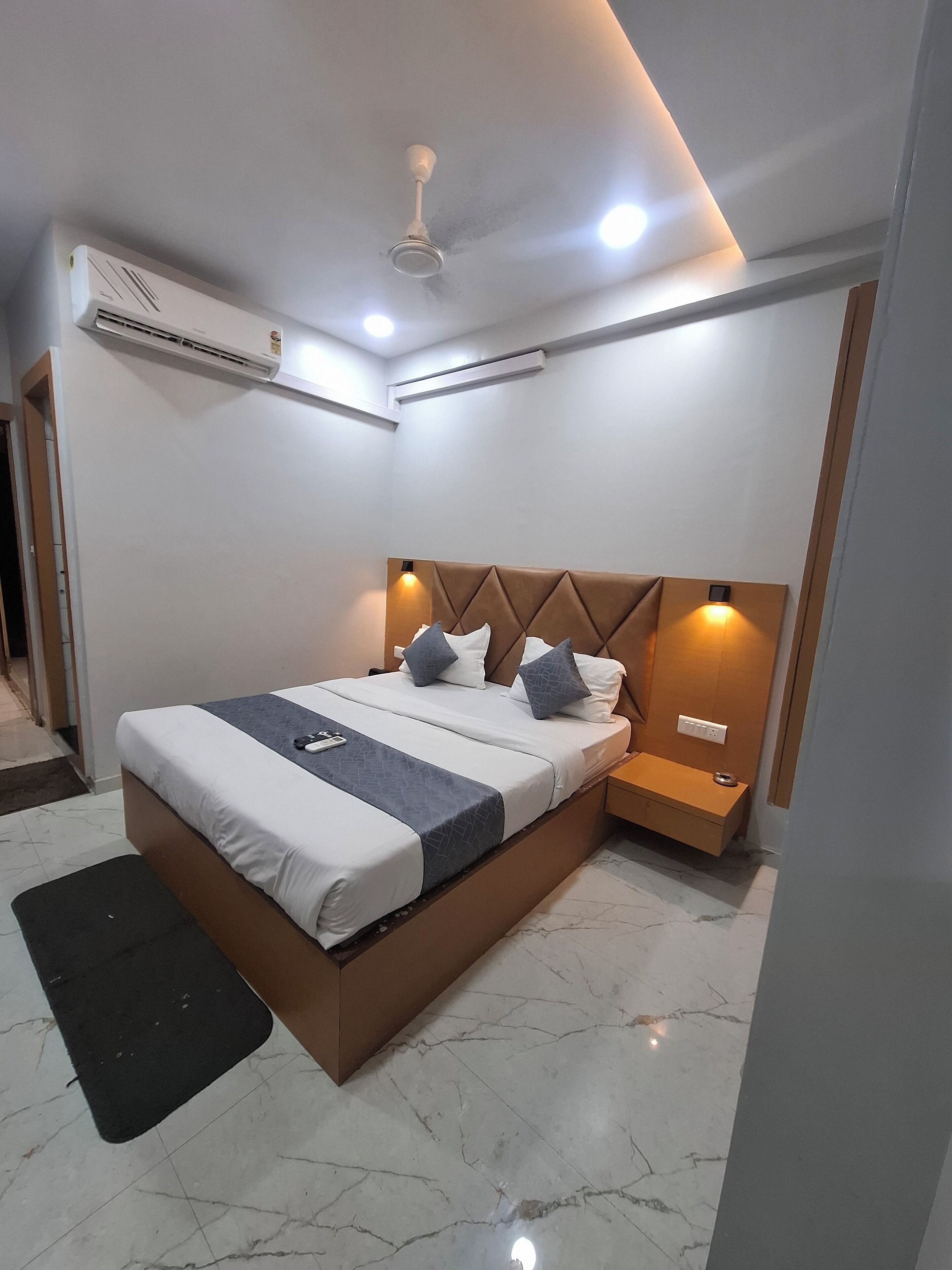 Une chambre moderne avec un grand lit, une tête de lit en bois, des lampes de chevet, un appareil de climatisation et un sol en marbre.