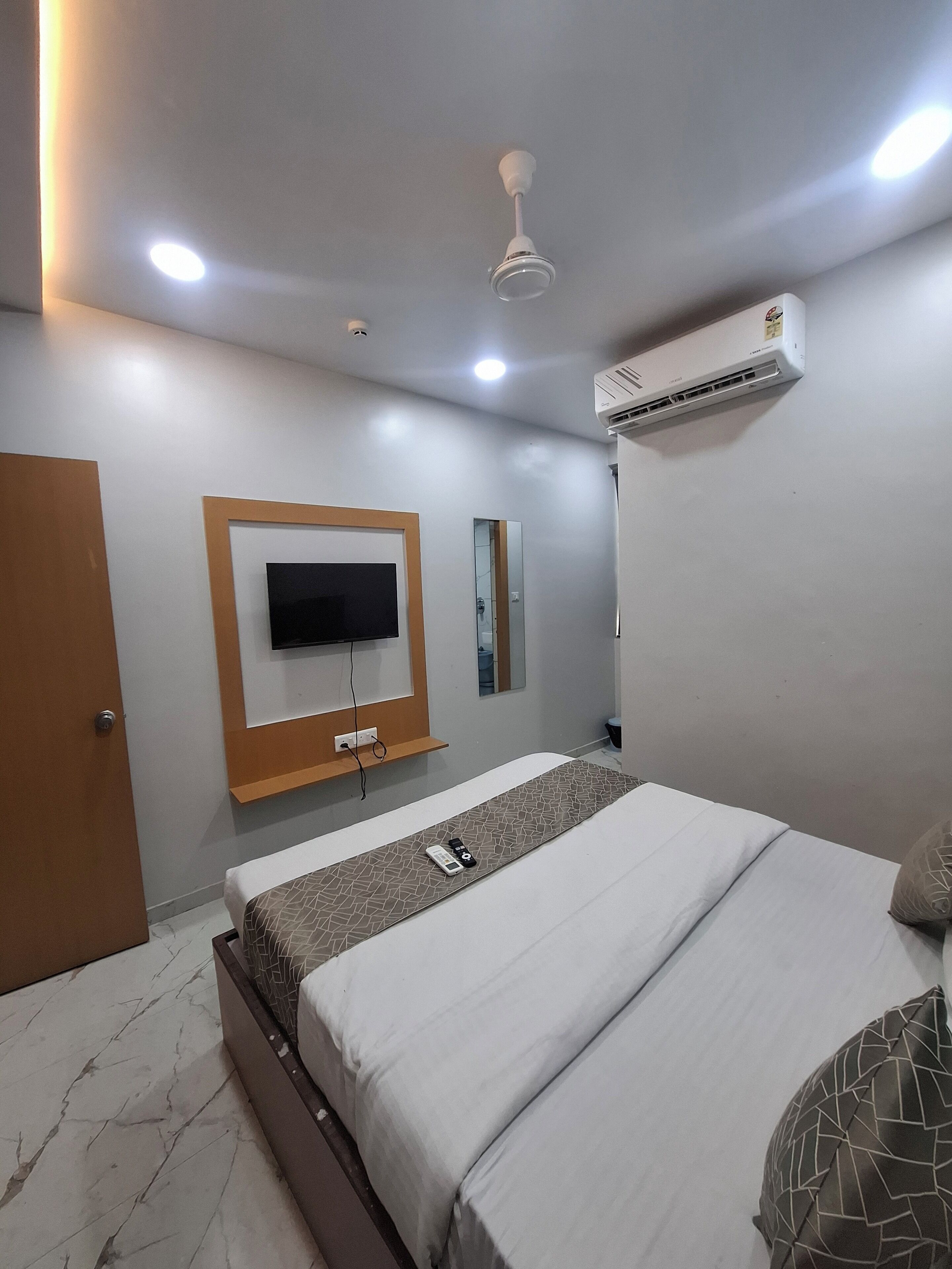 Une chambre d’hôtel moderne équipée d’un lit, d’un téléviseur fixé au mur, d’un climatiseur et d’un ventilateur de plafond.