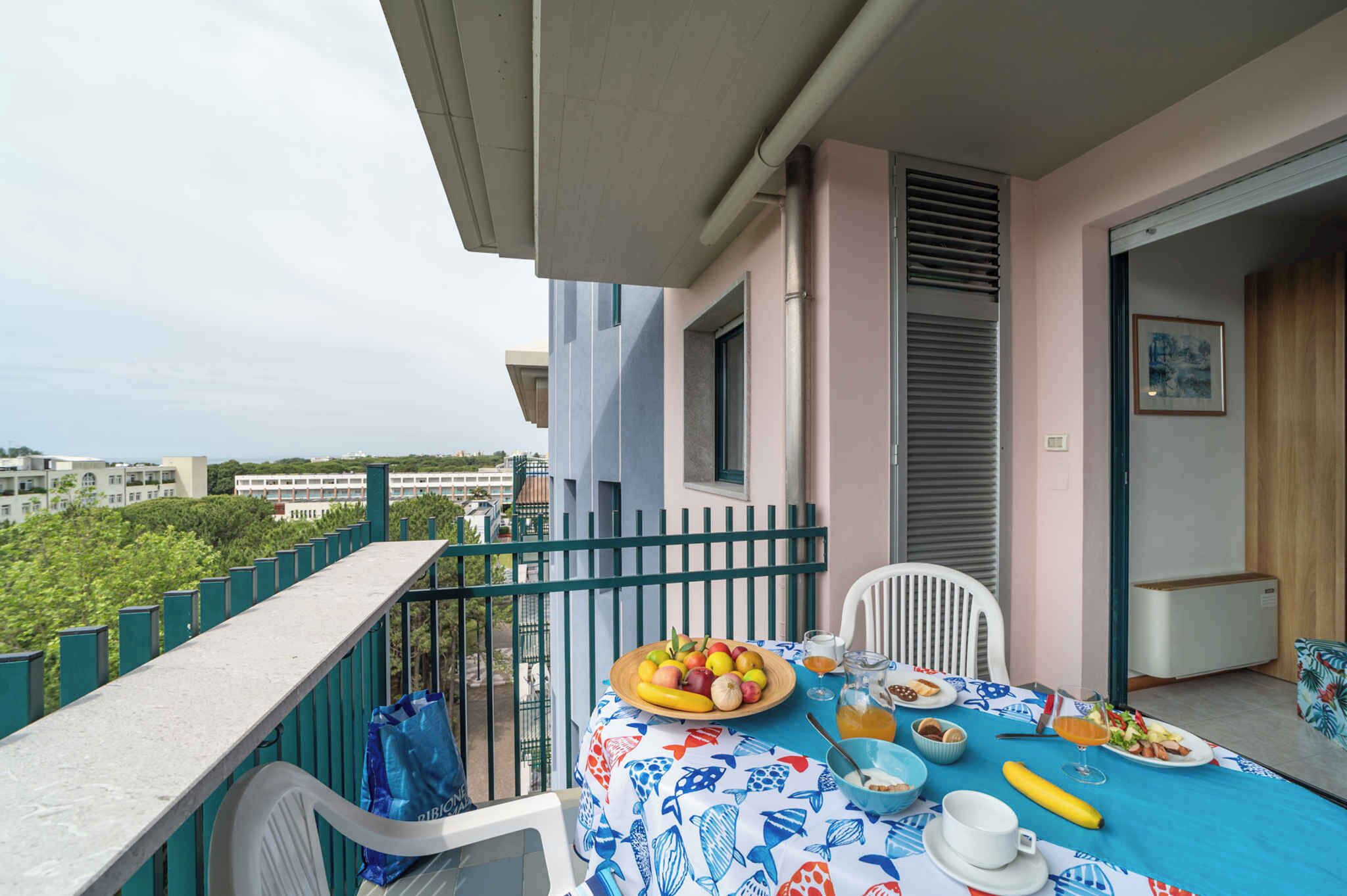 A balcony with a table set for breakfast, a chair, and a view of buildings and greenery.