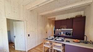 Une cuisine compacte aux murs en bois et dotée d’un îlot central, équipée d’appareils électroménagers modernes et de tabourets de bar.