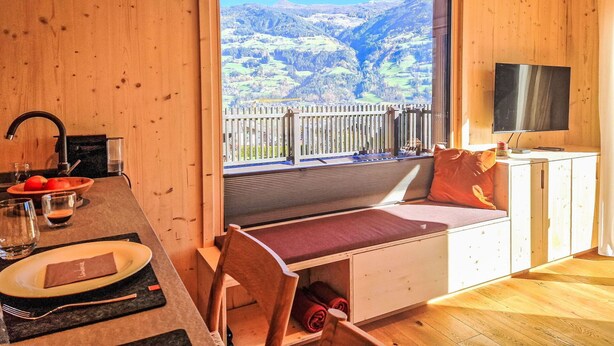 Une cabane en bois comprenant un coin repas, un téléviseur et un balcon avec vue sur la montagne.