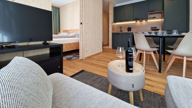 Et moderne, kompakt opholdsrum med fjernsyn, sofa, spiseplads og tekøkken.