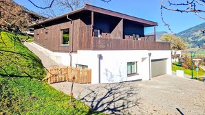 Et moderne hus med to etager og en balkon, beliggende på en skråning med udsigt over det omkringliggende landskab.