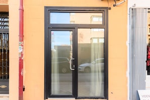 Ein Gebäude mit einer Glastür in Schwarzrahmen, einer roten Stange mit Aufklebern und einem Metallgitter.